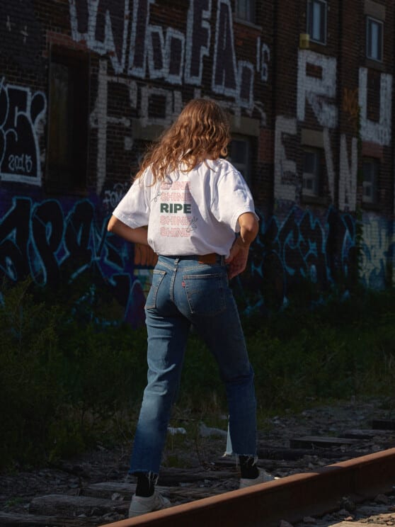 woman walking down the tracks in a ripe logo shirt