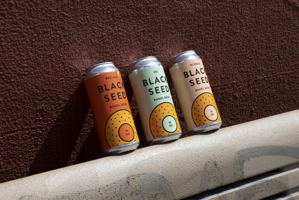 three cans of black seed bagels branded beer leaning against a wall
